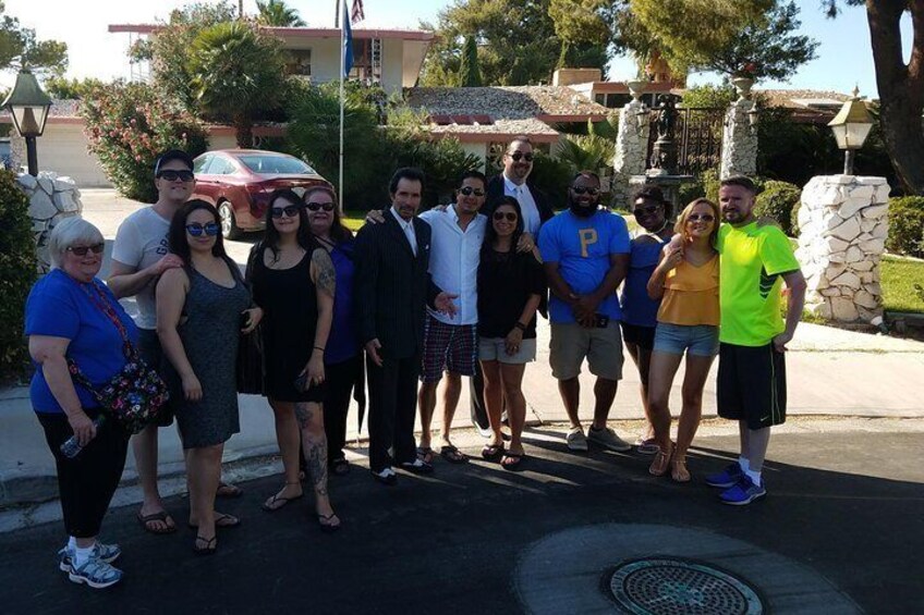 Un grupo de personas posando para una foto en una calle con un muro de piedra y un coche rojo al fondo. 5