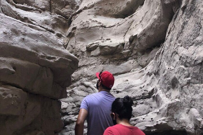 Una persona con gorra roja y una mujer con camisa morada caminando por un cañón estrecho con paredes rocosas. 1