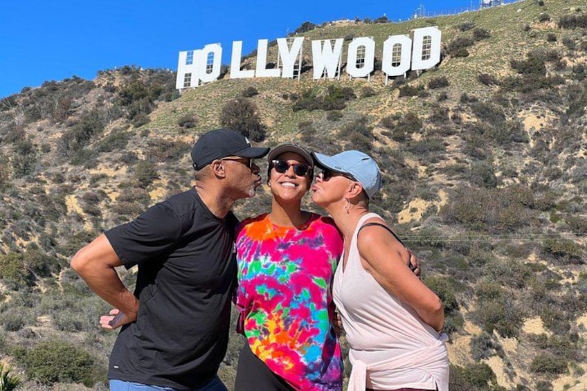 Three people standing in front of the Hollywood sign with a hilly landscape in the background. 2