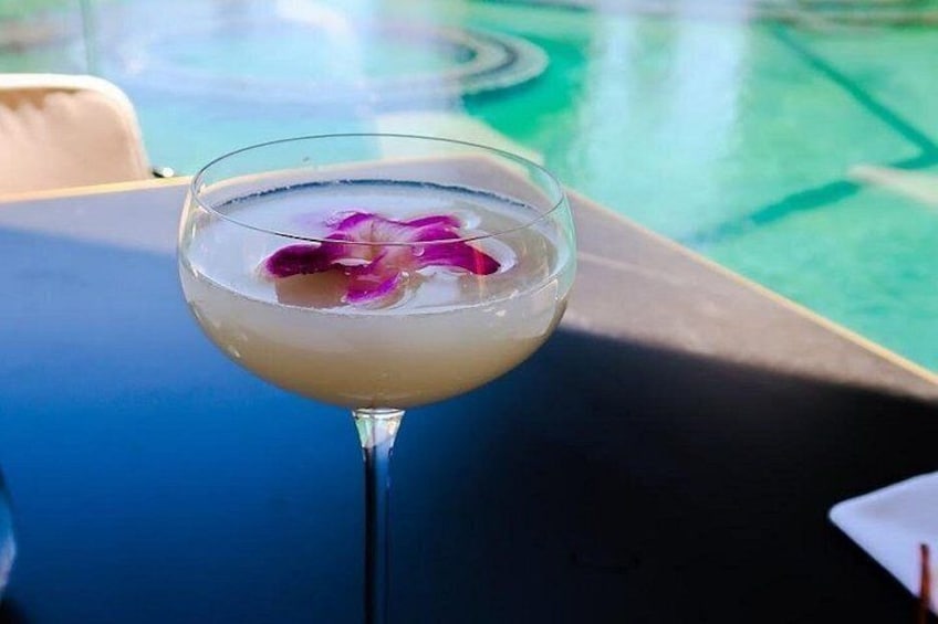 A cocktail glass with a flower on a table near a pool. 4