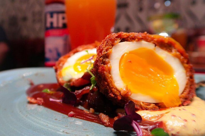 A Scotch egg with a soft-boiled egg inside, served on a plate with sauce and greens. 3