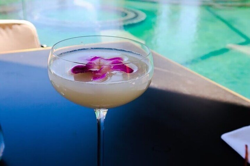A cocktail with a purple flower garnish on a table by a pool. 2