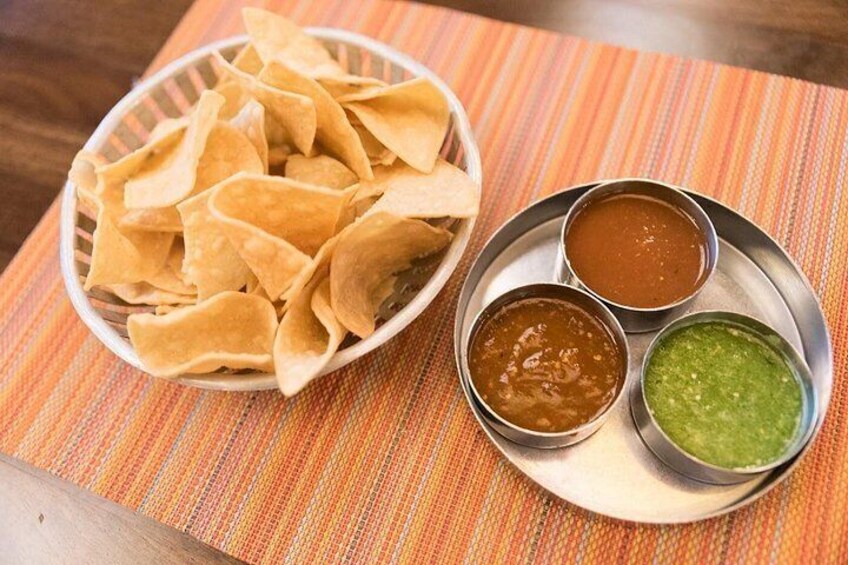 A bowl of tortilla chips, two small bowls of dips, and a metal plate on a striped tablecloth. 5