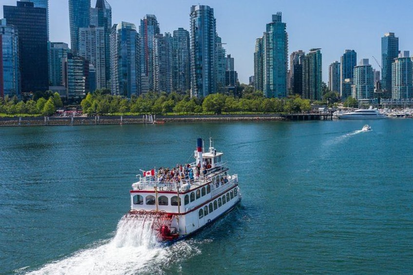 A white riverboat with passengers, moving through a river with a city skyline in the background. 1