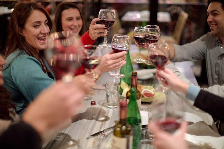 Un grupo de personas brindando con copas de vino en una mesa con botellas y vasos. 2