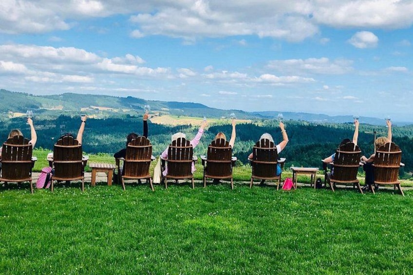 Un grupo de personas sentadas en sillas Adirondack sobre una colina cubierta de césped, con una vista panorámica de un valle y colinas al fondo. 4