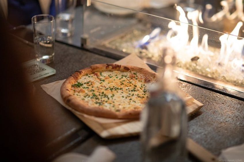 Une pizza servie sur une planche en bois, accompagnée d’un verre d’eau et d’une bougie en arrière-plan. 2