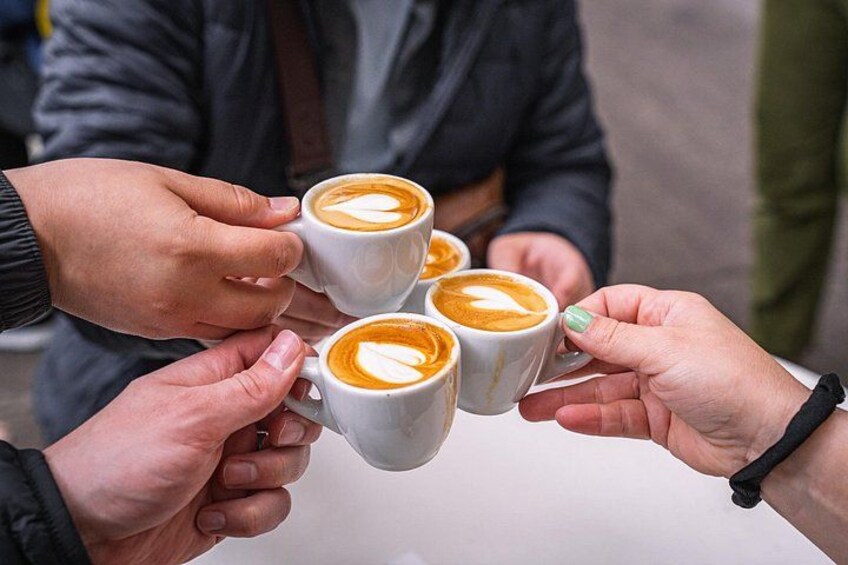 Fyra personer håller i kaffemuggar med lattekonst. 1