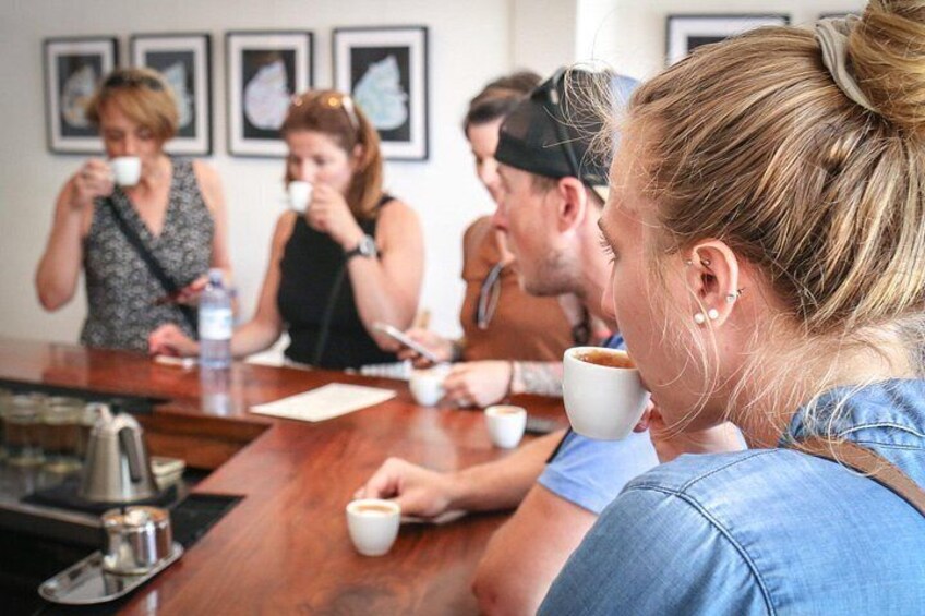 Un grupo de personas sentadas en una mesa de madera, cada una sosteniendo una taza blanca, probablemente tomando café. 2