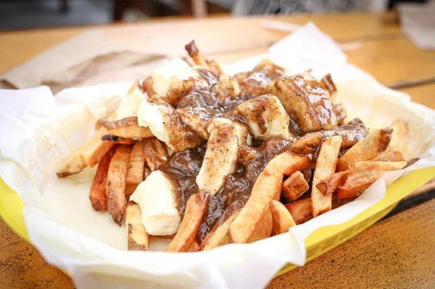 A serving of poutine with fries and cheese curds on a paper-lined tray. 2