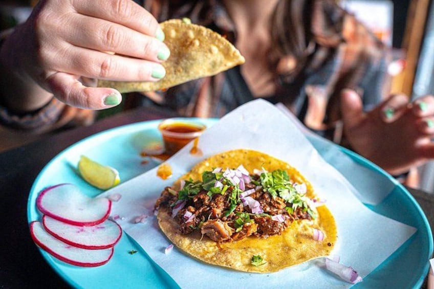 A person holding a tortilla chip over a plate with a food item topped with onions and green herbs. 3