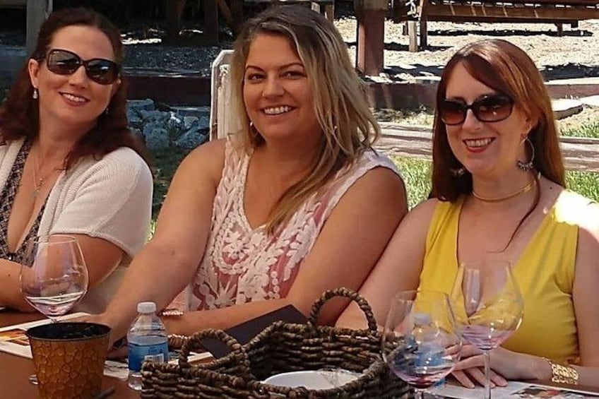 Three people sitting at an outdoor table with drinks and a woven basket. 2