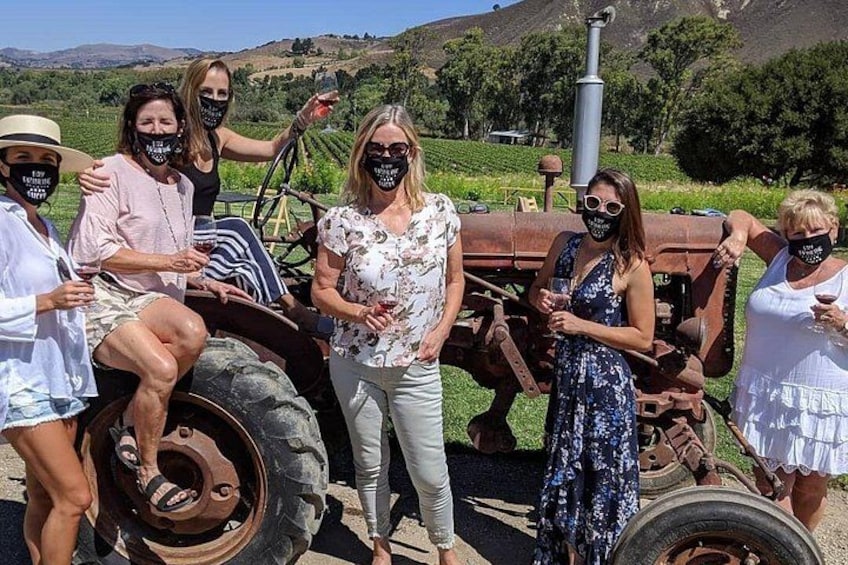 A group of people standing in front of a vintage tractor in a vineyard. 2