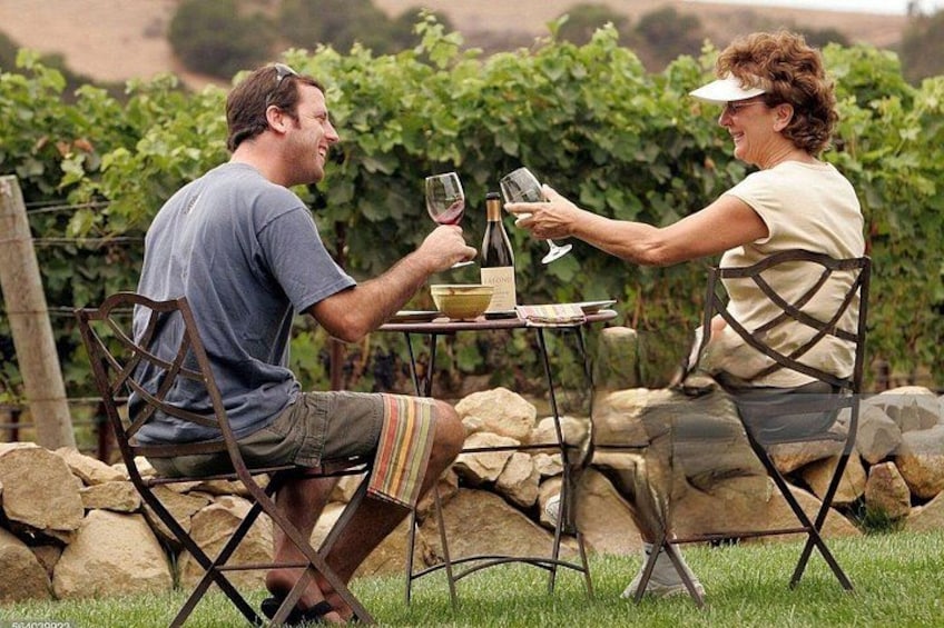 Two people sitting at a table outdoors with a bottle of wine and glasses. 5