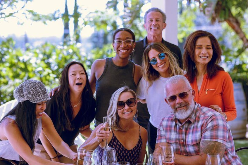Un groupe de personnes est assis à une table à l’extérieur, devant des boissons, et est entouré de verdure. 2