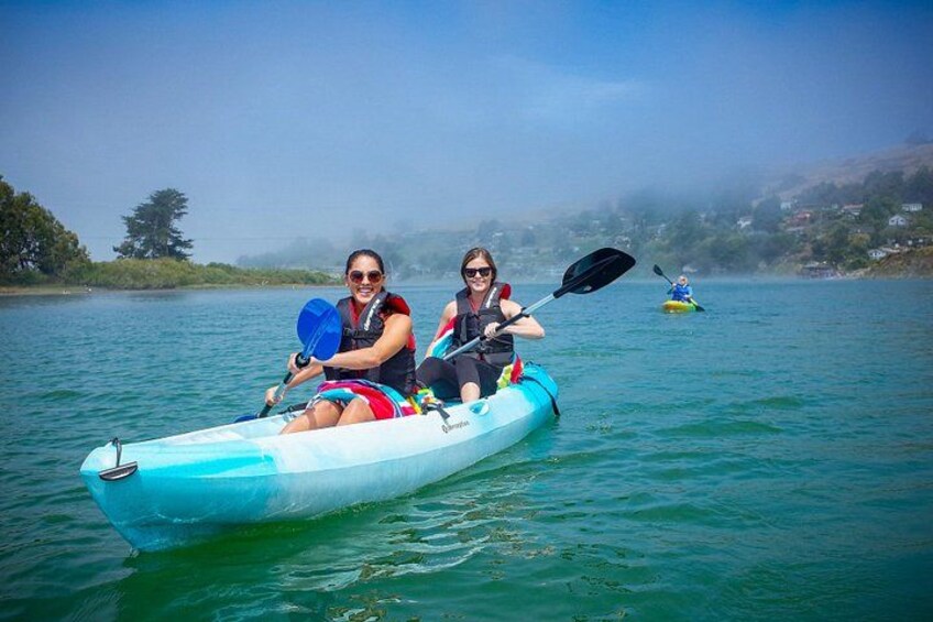 Two people kayaking on a calm lake with a distant kayaker. 1