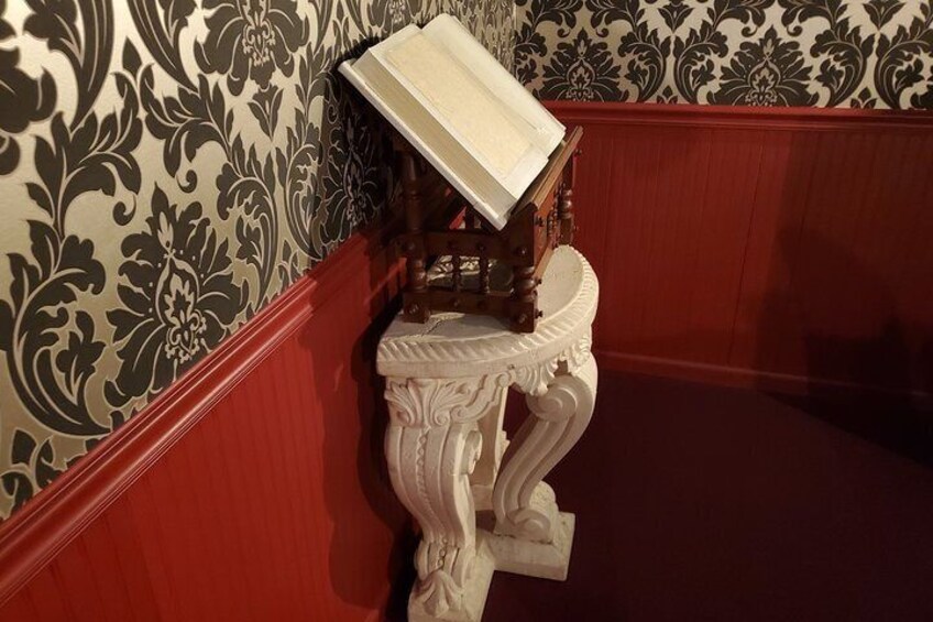 Een witte, decoratieve tafel met een houten blad in een kamer met behang met een patroon en rode lambrisering. 5