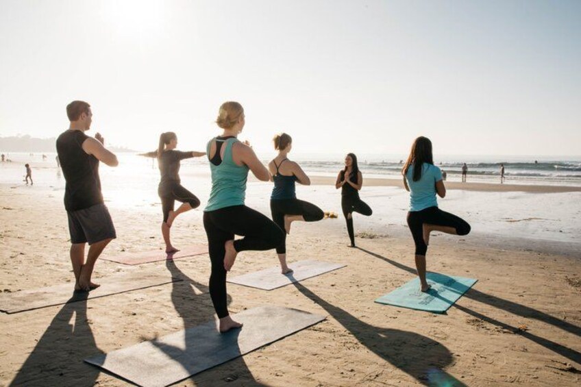 Un grupo de personas practicando yoga sobre esterillas en una playa. 1