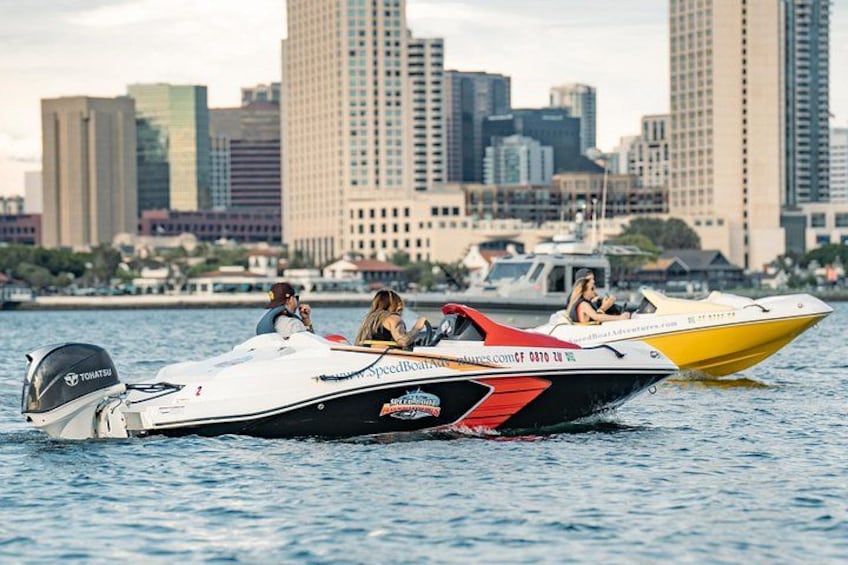 A speedboat with two passengers on the water, a city skyline in the background, and a calm sea. 2