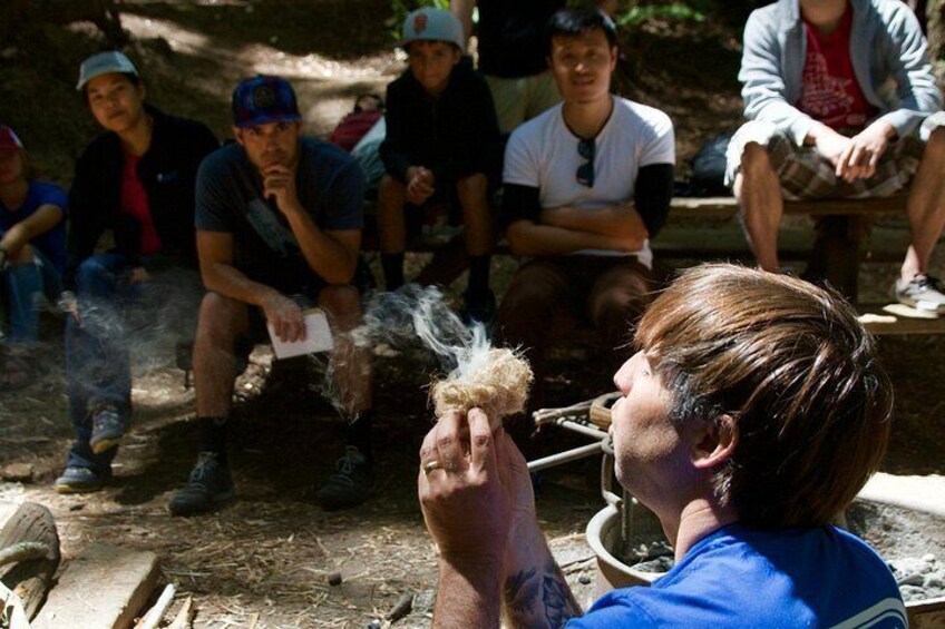 Una persona sosteniendo una pluma, con un grupo de personas sentadas alrededor de una fogata en un área boscosa. 2
