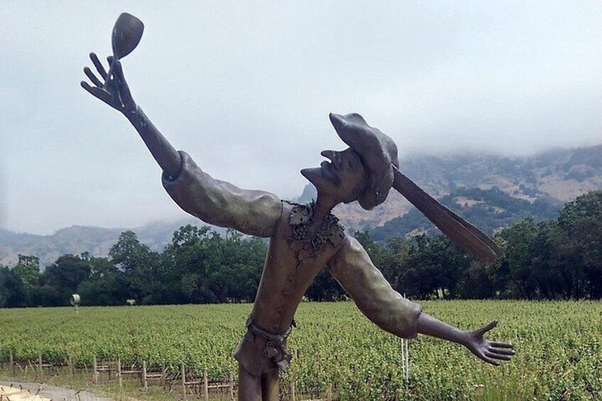 A statue of a figure with a hat and a tool, standing in a field with a mountainous background. 5