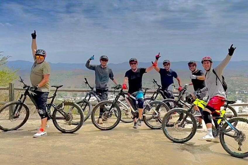 A group of cyclists posing with their bikes on a concrete ledge with a scenic view in the background. 1