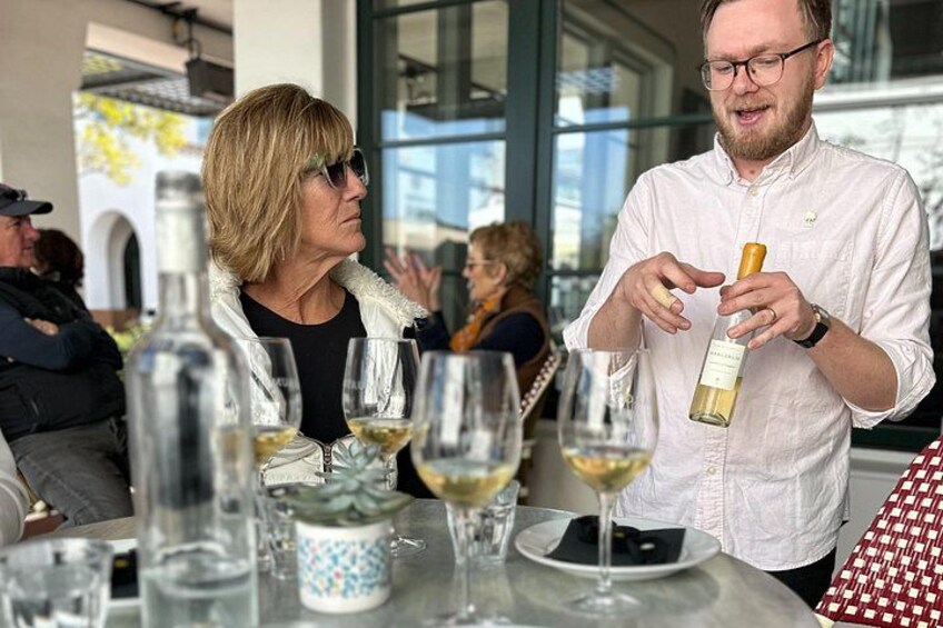 Eine Person gießt Wein in ein Glas an einem Tisch mit weiteren Weingläsern und Flaschen. 3