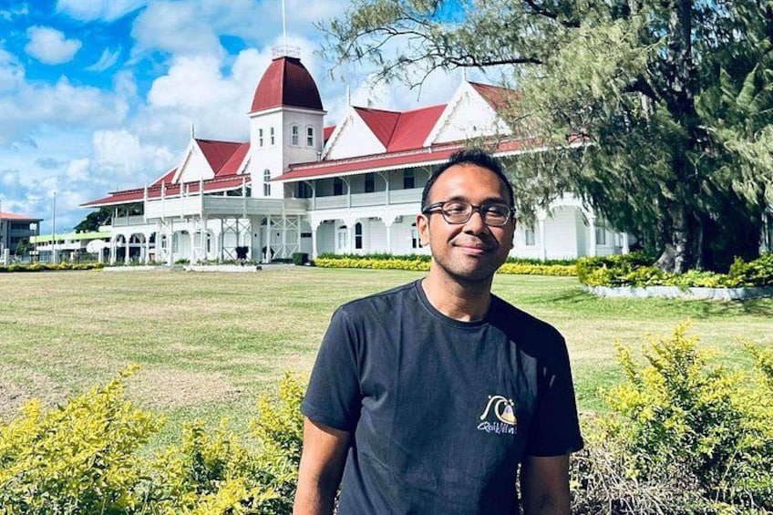A man standing in front of a large white building with a red roof and a tower. 1