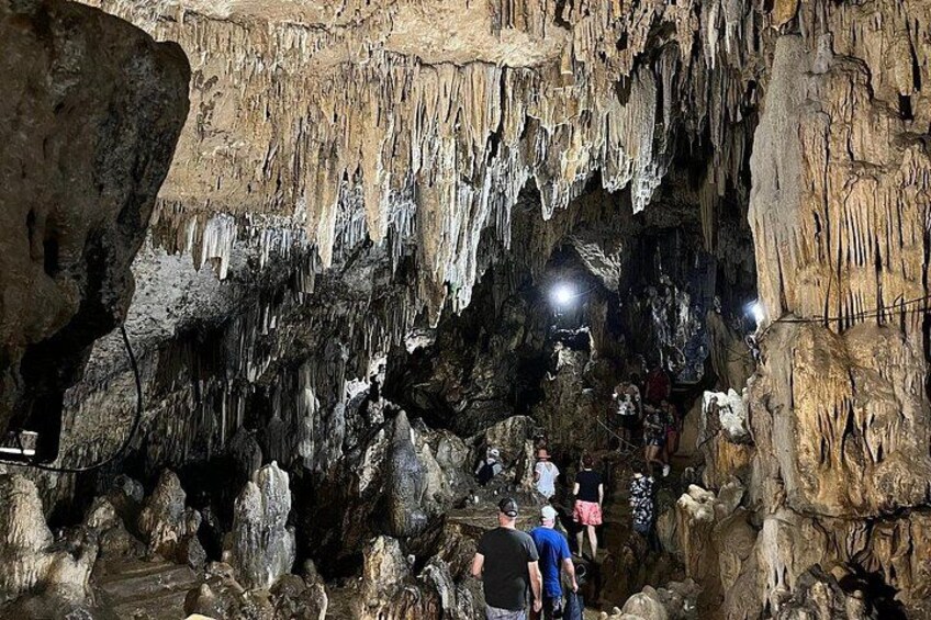 A cave with stalactites and stalagmites, people exploring, and artificial lighting. 5