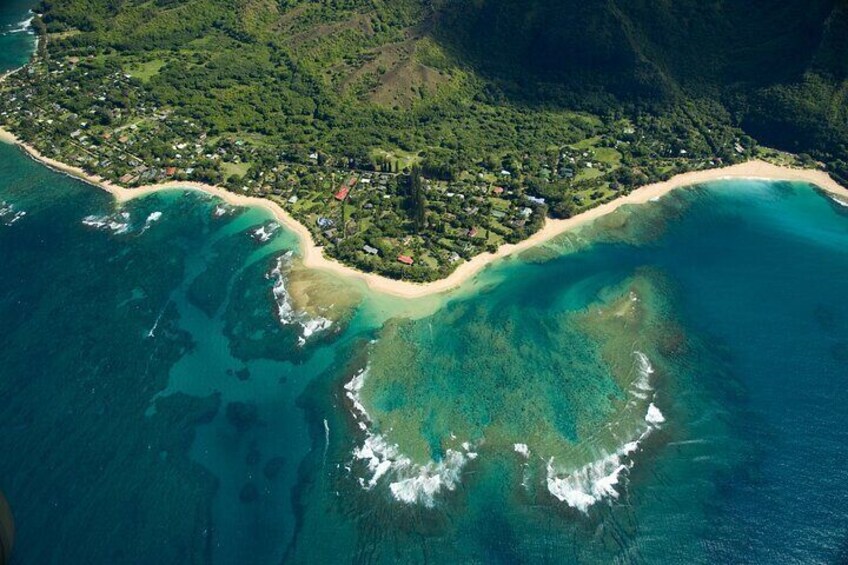 An aerial view of a coastal area with a beach, clear blue waters, and a densely vegetated inland area. 5