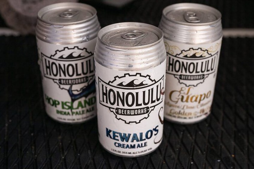 Tres latas de cerveza Honolulu Beerworks sobre una superficie texturizada. 3