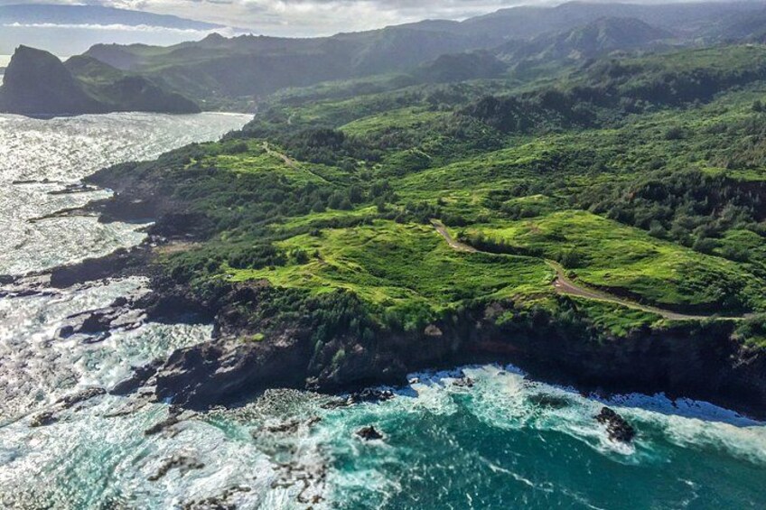 A coastal landscape with a winding road, lush green hills, and a rocky coastline. 4