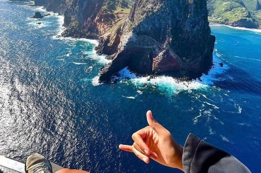 A hand making a peace sign, a rocky coastline, and the ocean. 2