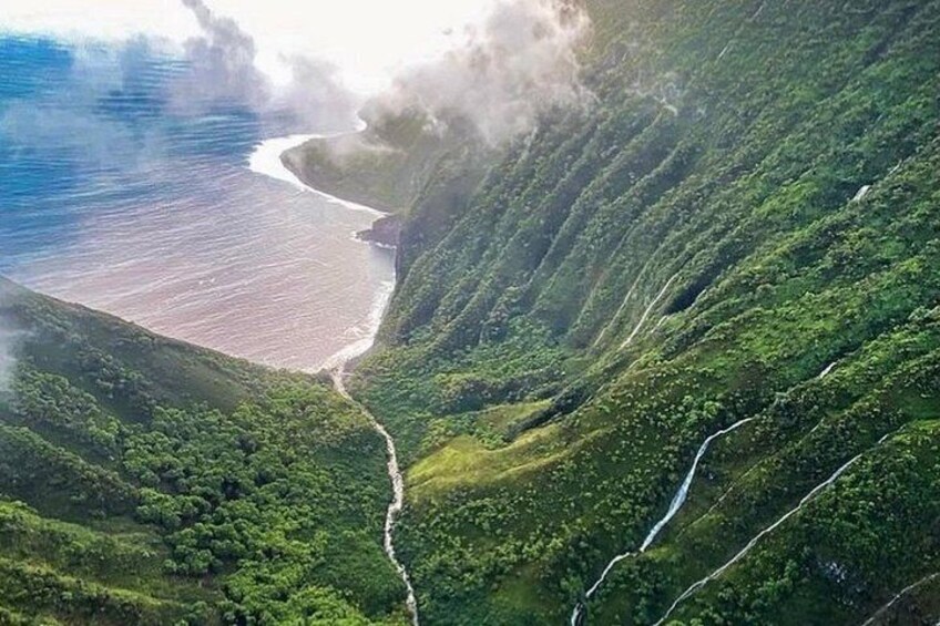 A coastal landscape with a winding road, lush green hills, and a beach. 3