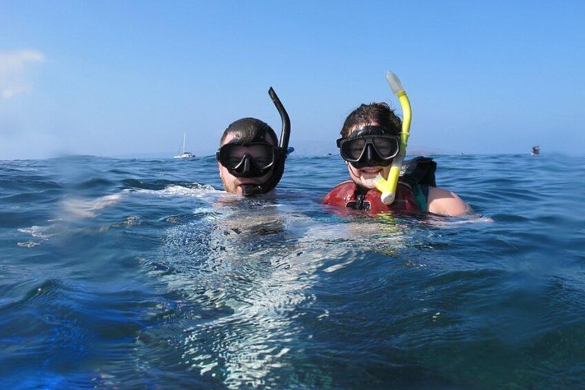 Twee mensen snorkelen in helderblauw water, met een zeilboot op de achtergrond. 2