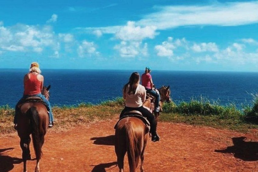 Tres personas montando caballos por un sendero de tierra con vista al océano. 2