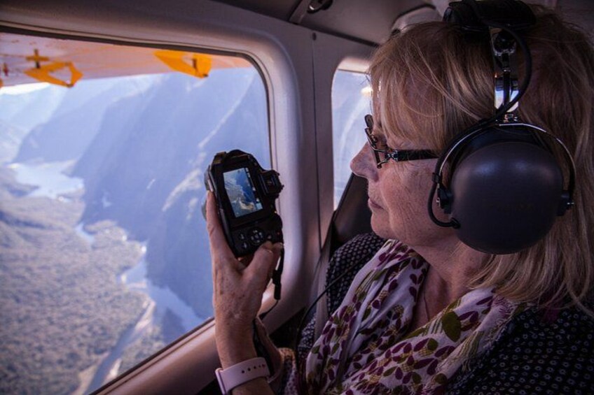 A person taking a photograph with a camera, wearing headphones, and looking out a window at a mountainous landscape. 5