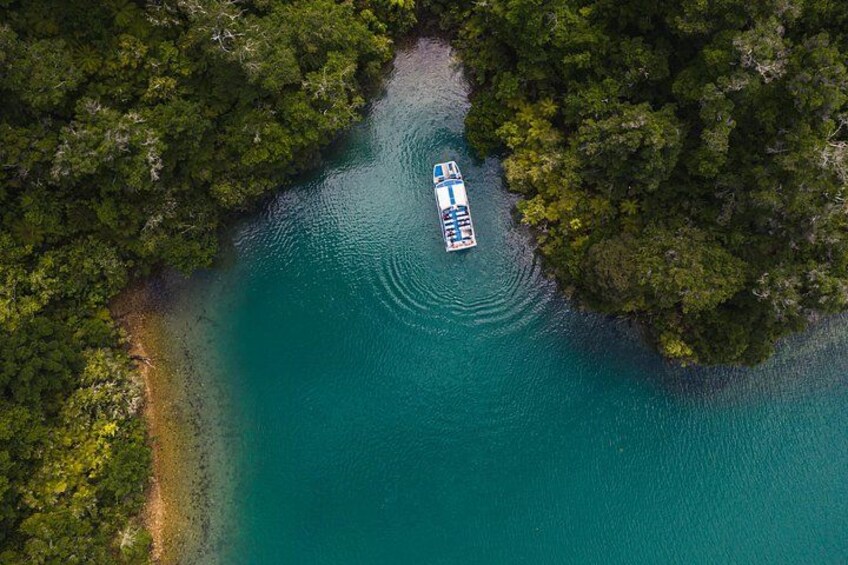 Vue aérienne d’un bateau sur une rivière turquoise, entourée d’une forêt verdoyante et dense. 5