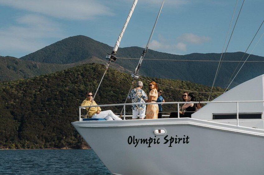 A boat named Olympic Spirit on calm waters with a mountainous backdrop. 1