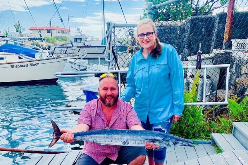En person håller i en stor fisk på en brygga, med båtar i bakgrunden. 4