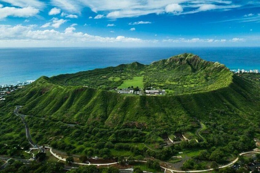 A lush green hill with a small building on top, surrounded by a winding road and a view of the ocean. 3