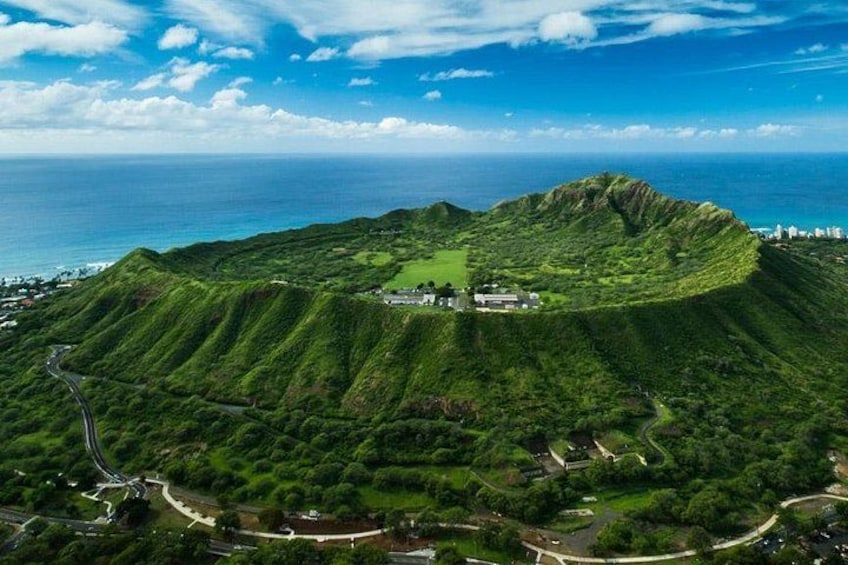 A lush green hill with a small building on top, surrounded by a winding road and a view of the ocean. 4