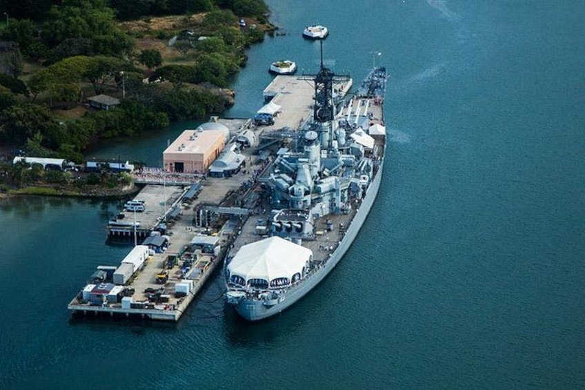 A large naval ship docked at a pier with a small island nearby. 3