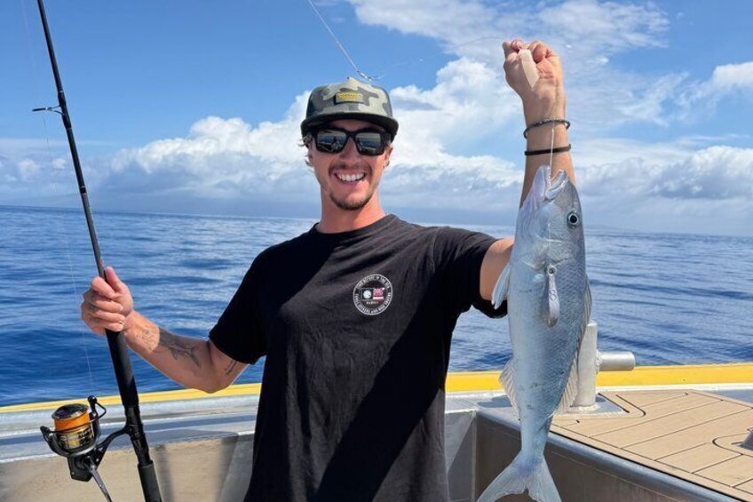En person holder en fisk om bord på en båd med oceanen i baggrunden. 3