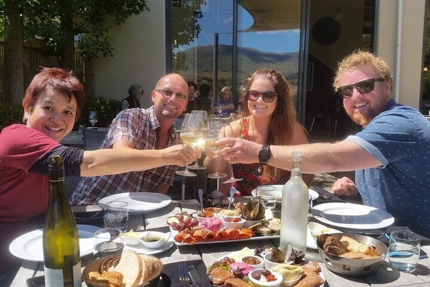 Un grupo de personas brindando con copas de vino en una mesa de comedor al aire libre con varios platos. 5