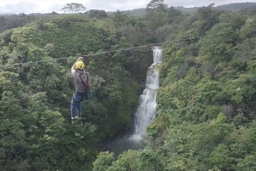 A person standing on a zip line over a lush forest with a waterfall in the background. 3
