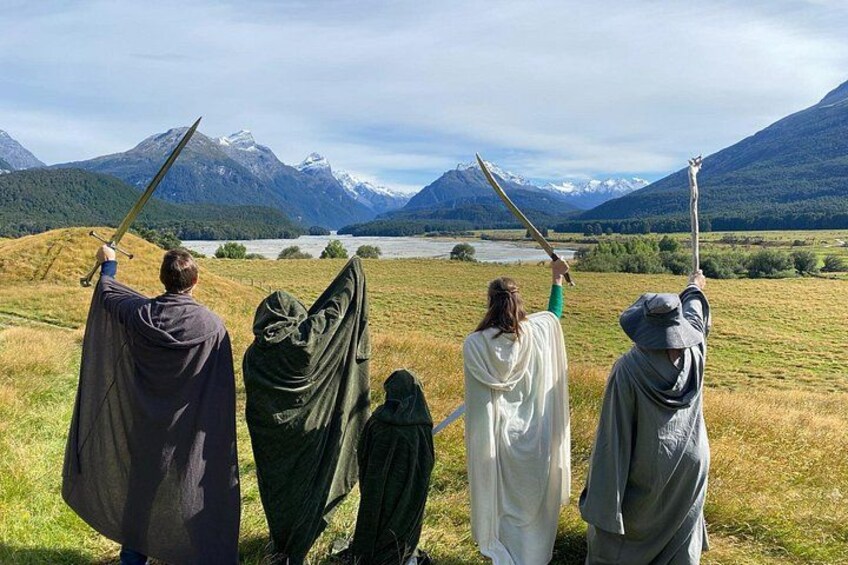 Vier Personen in historischen Kostümen mit Schwertern stehen auf einer Wiese, im Hintergrund sind Berge zu sehen. 3