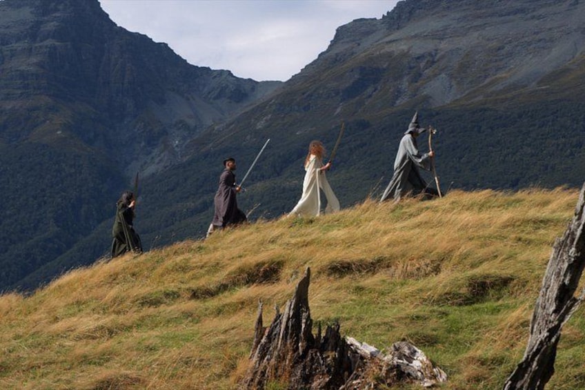 Eine Gruppe von Menschen in mittelalterlichen Kostümen auf einer grünen Hügelkuppe, im Hintergrund Berge. 1
