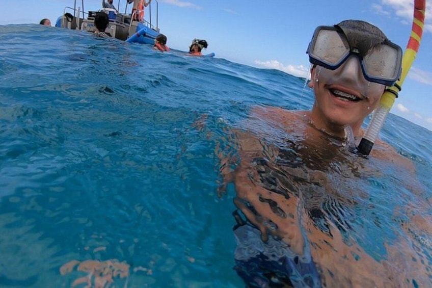 A person snorkeling in clear blue water with a boat in the background. 2