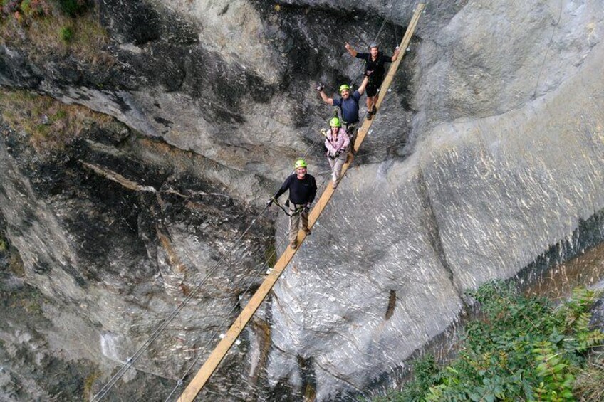 People walking on a narrow wooden plank over a rocky cliff. 3